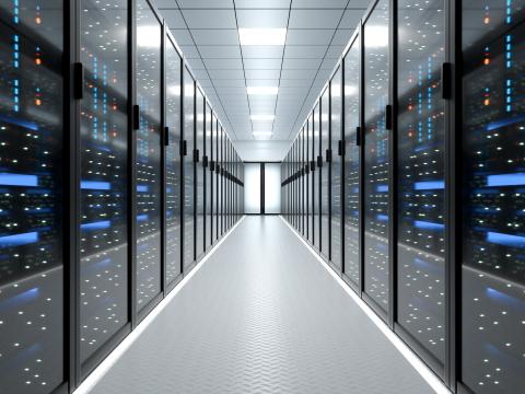 Interior view of a modern data center with rows of server racks on both sides of a brightly lit corridor. The server racks feature illuminated indicators and reflective glass doors.