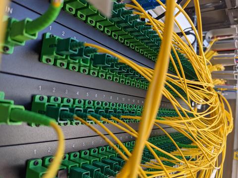 Close-up view of a fiber optic patch panel with numerous yellow fiber optic cables connected to green LC connectors in a structured and labeled network rack.