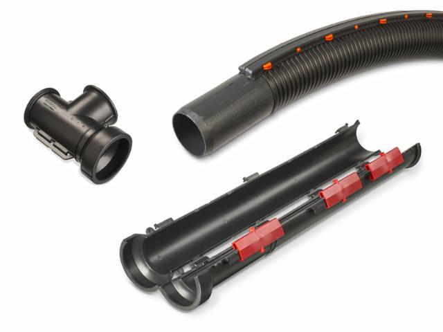 Black cable protection accessories including a flexible corrugated conduit, a T-connector, and a split conduit with red locking clips, used for securing and routing cables in underground or industrial installations.