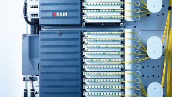 Fiber optic distribution frame by Reichle & De-Massari, featuring multiple rows of green LC connectors and yellow patch cords neatly routed to the side, used for structured fiber management in a telecom or data center environment.