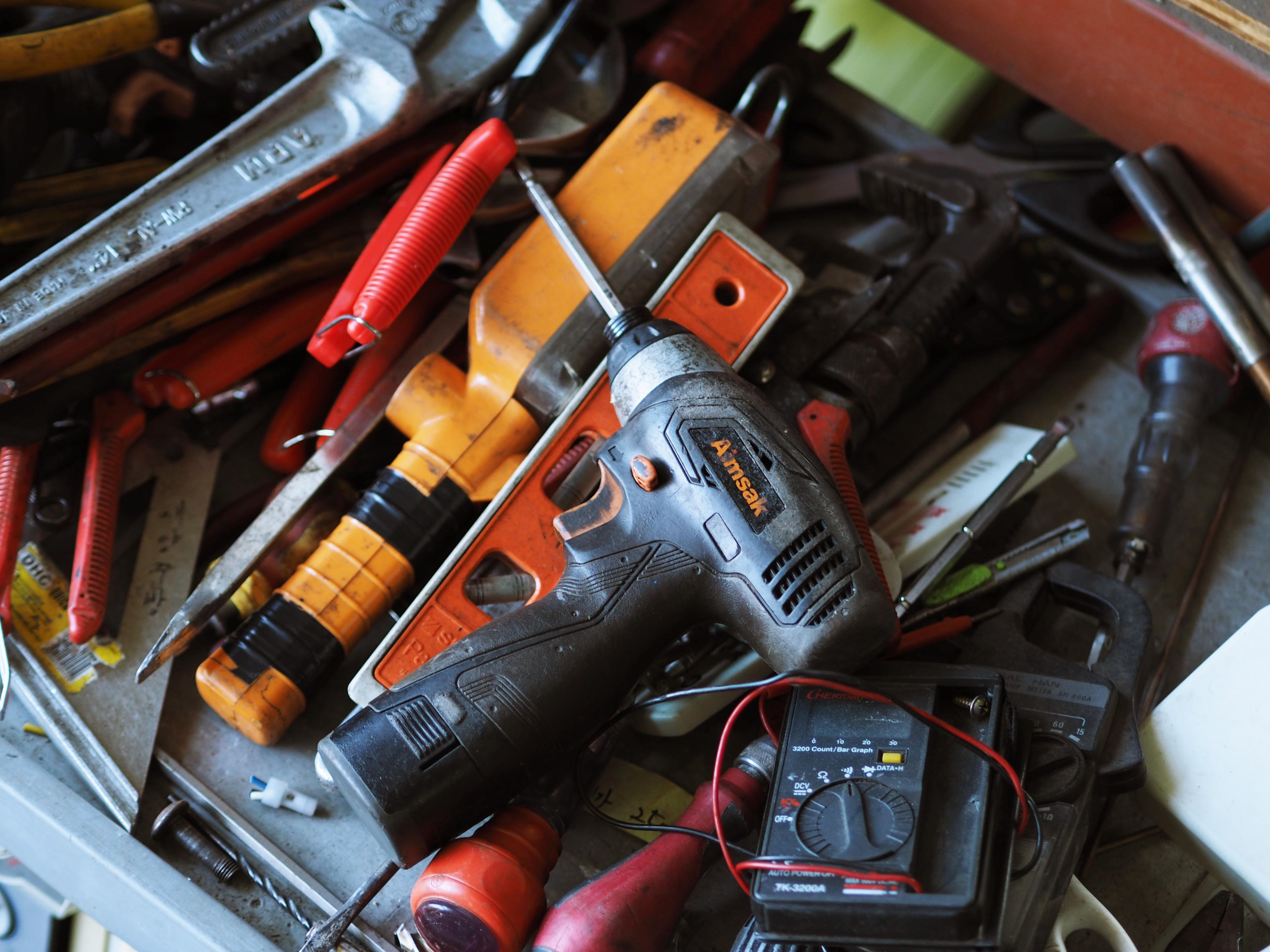 A cluttered toolbox filled with various hand tools, including a cordless drill, screwdrivers, wrenches, a voltage meter, and other maintenance equipment.