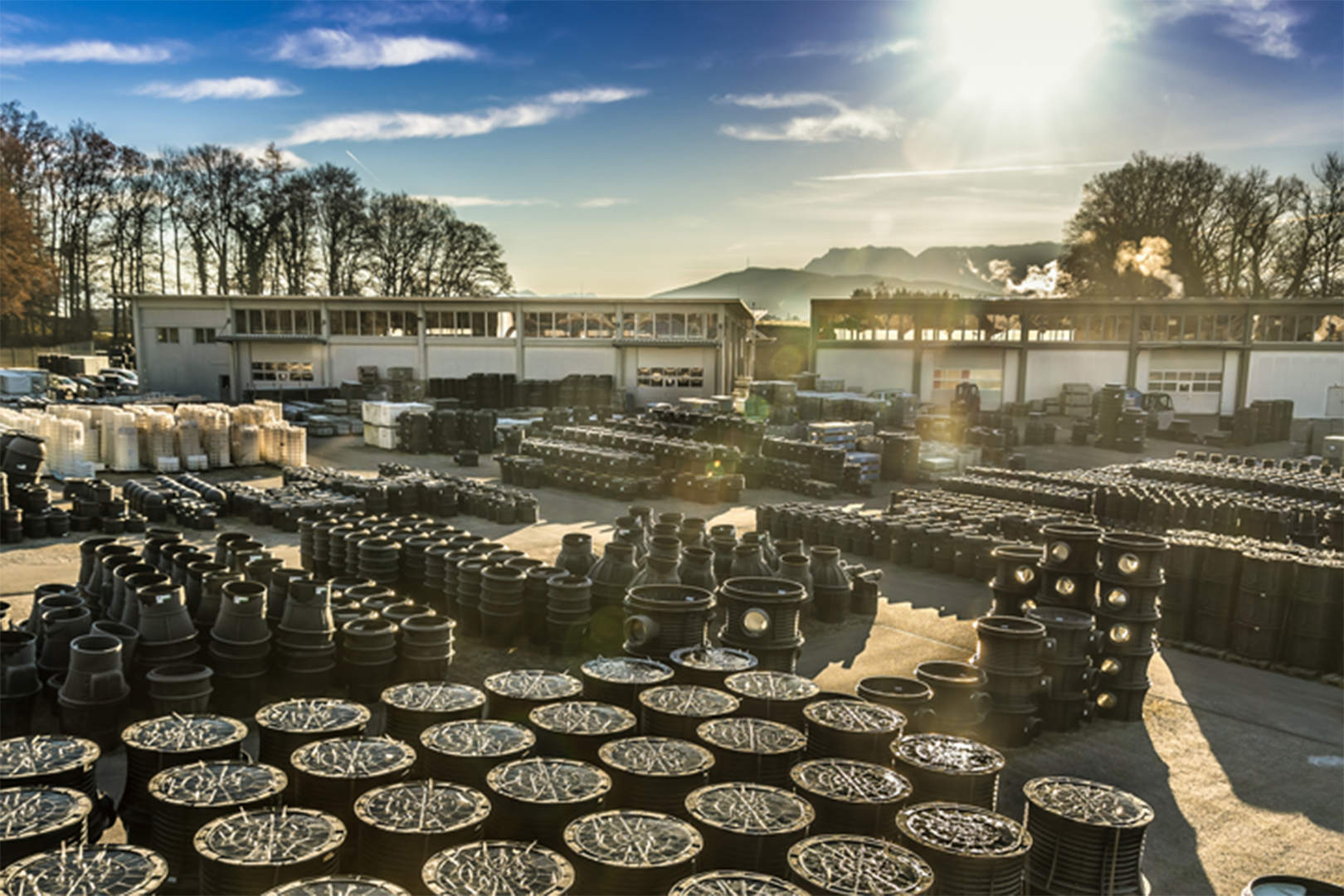 Outdoor industrial storage area with hundreds of large black cable drums neatly arranged, surrounded by warehouses and buildings under a bright sunlit sky.