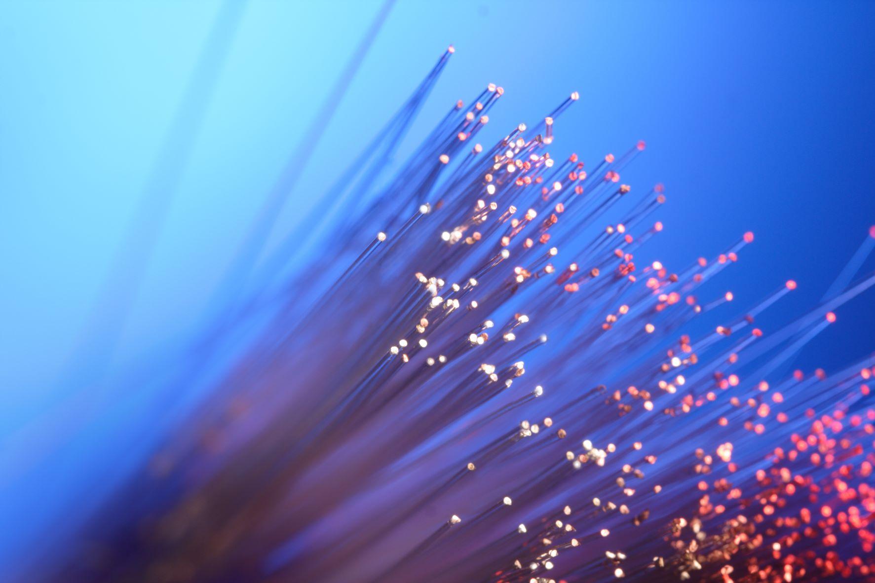 Close-up of illuminated fiber optic strands glowing in blue and red hues, representing high-speed data transmission.