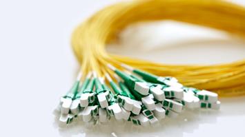 A coiled bundle of yellow fiber optic patch cables with green and white LC connectors neatly arranged at the ends, placed on a reflective white surface.